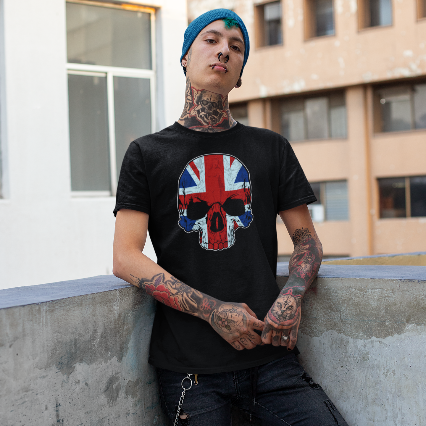 Person wearing a black t-shirt with a Union Jack design, sitting against a building.